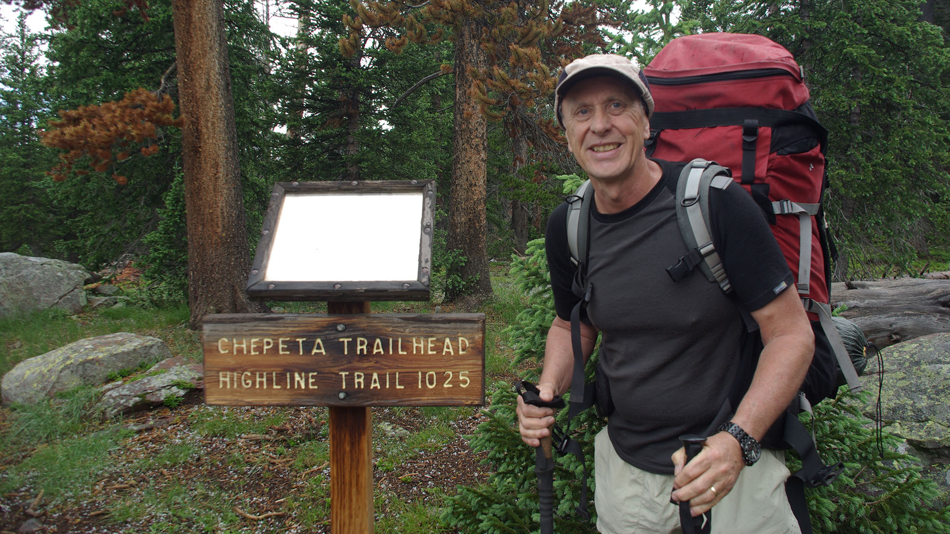 Eric Robinson, a hiker wearing a red backpack, stands in front of a sign reading Chepeta Trailhead.