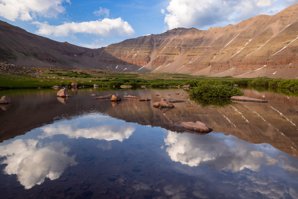 A small tarn reflects an image of a mountain, Kings Peak, in late afternoon light.