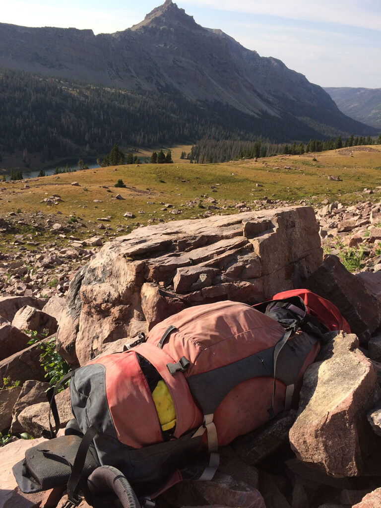A faded red backpack sits wedged against a rock in a mountain wilderness
