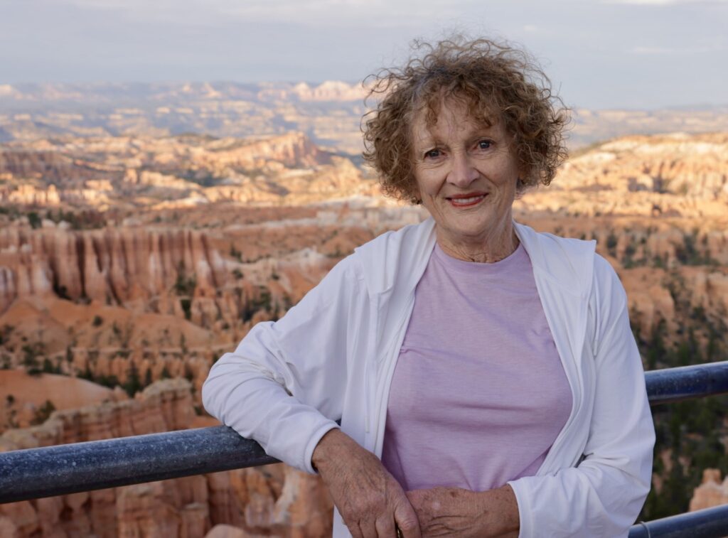 Woman in pink shirt and white jacket stands in front of desert scenery