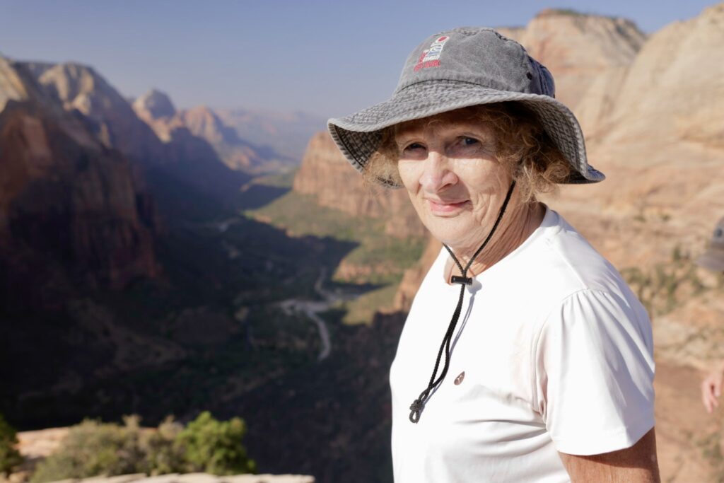 A woman in a floppy hat stands atop a cliff edge in Zion National Park