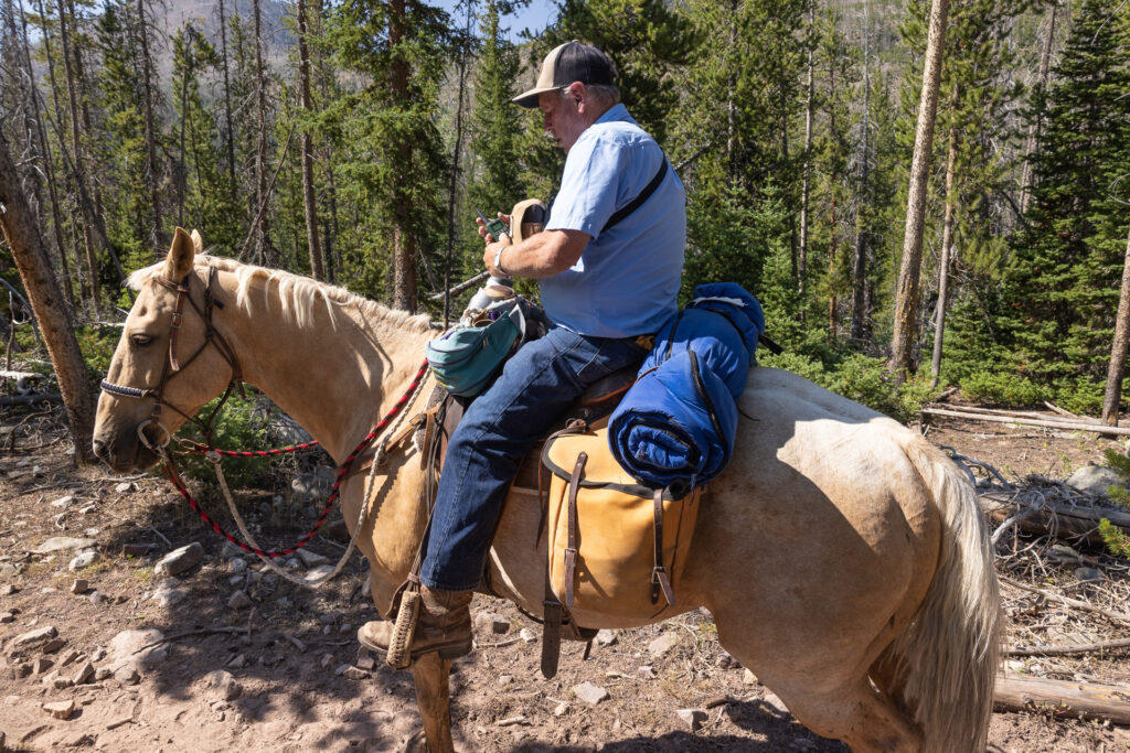 A man on horseback holds a small radio on a forested trail
