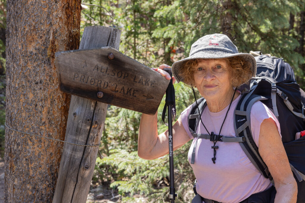 Marilyn Koolstra stands next to a wooden signboard pointing the way to Allsop Lake