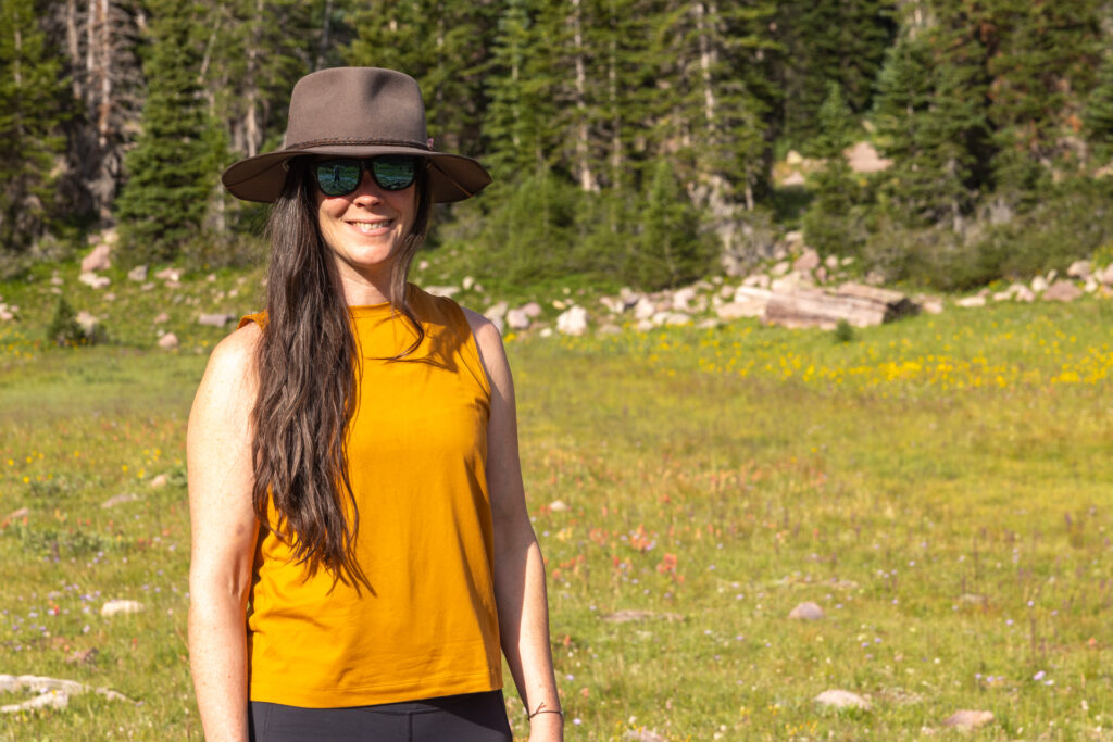 Julia Geisler stands in a meadow at the edge of a forest wearing an akubra